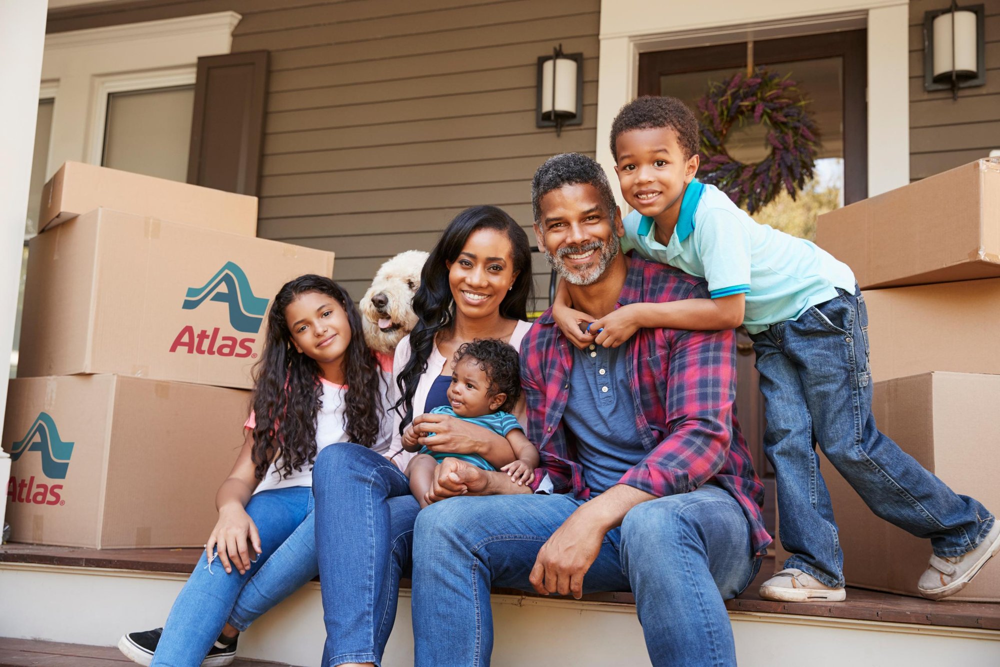 Family sitting on front porch among several Atlas moving boxes